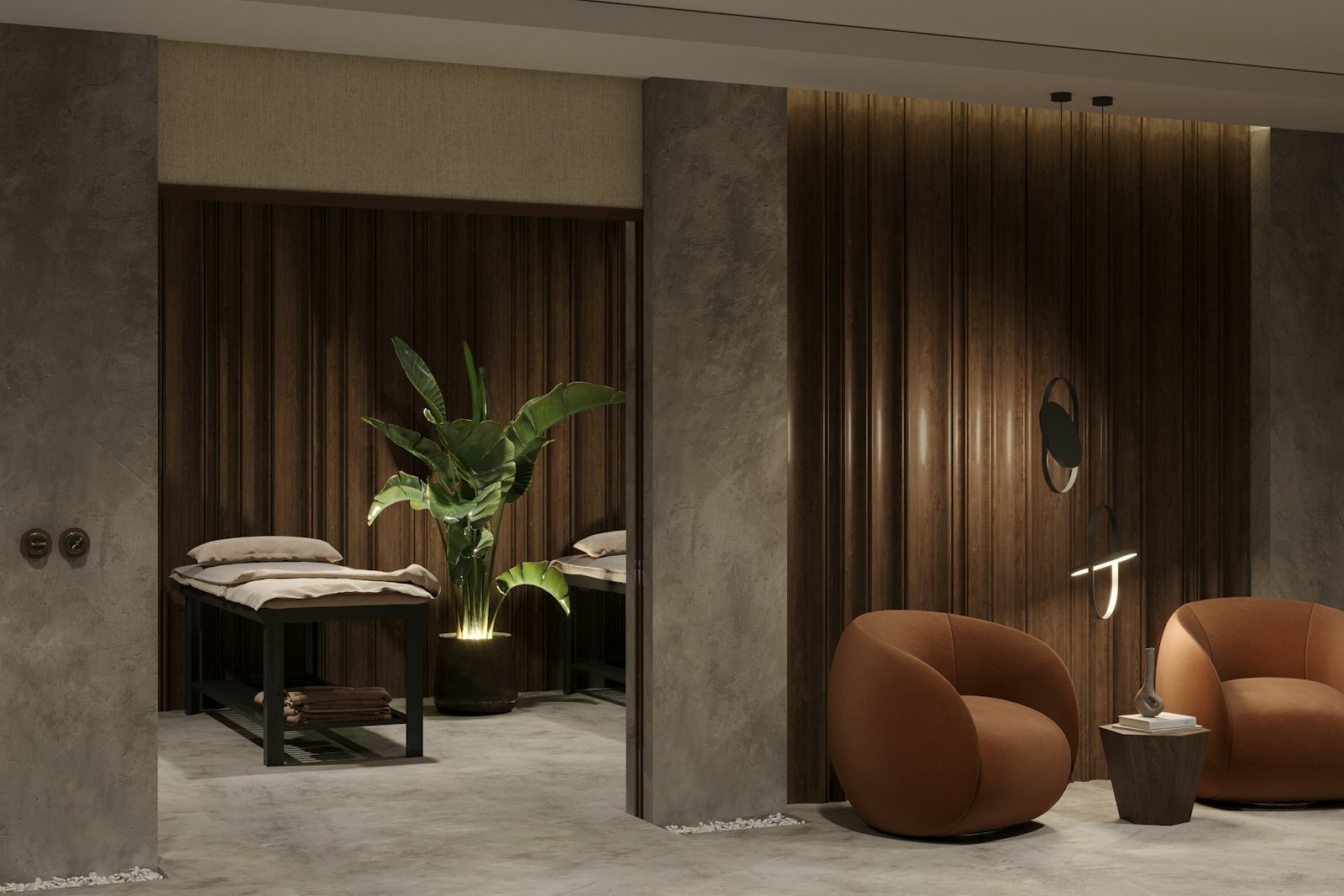 A softly lit spa lounge with dark timber walls, two rounded armchairs and a treatment bed beside a large plant.