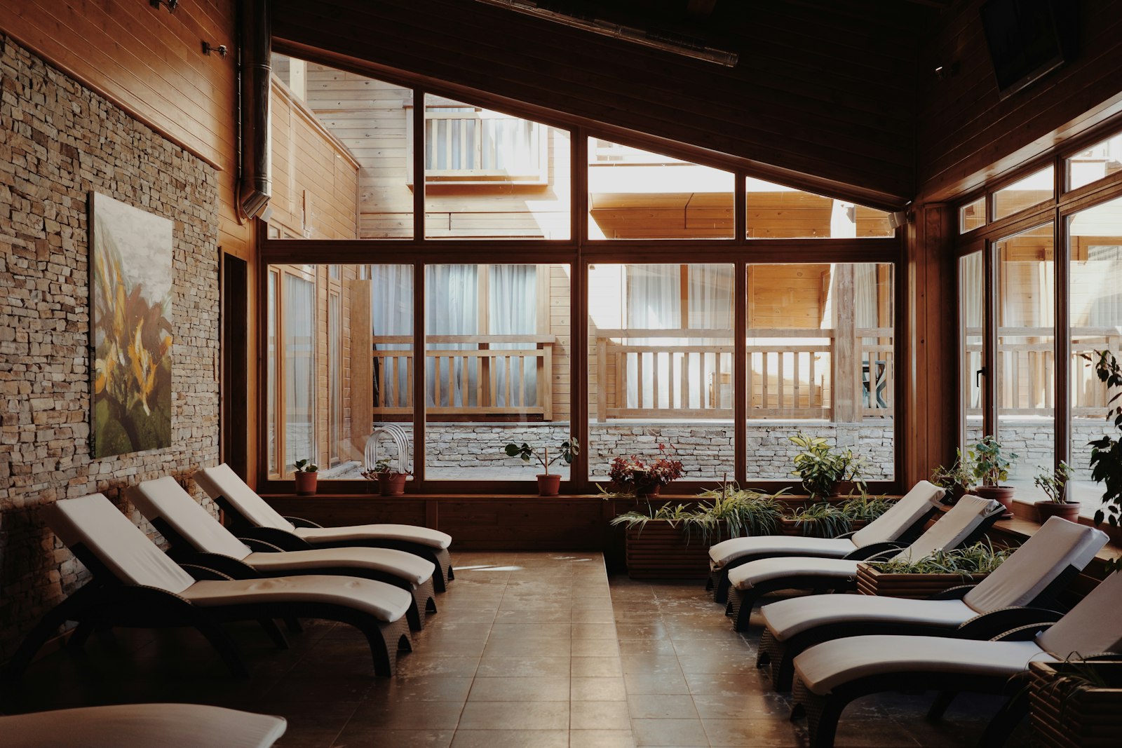 A quiet spa relaxation room with two rows of cushioned loungers, a stone wall and sunlight through tall timber-framed windows.